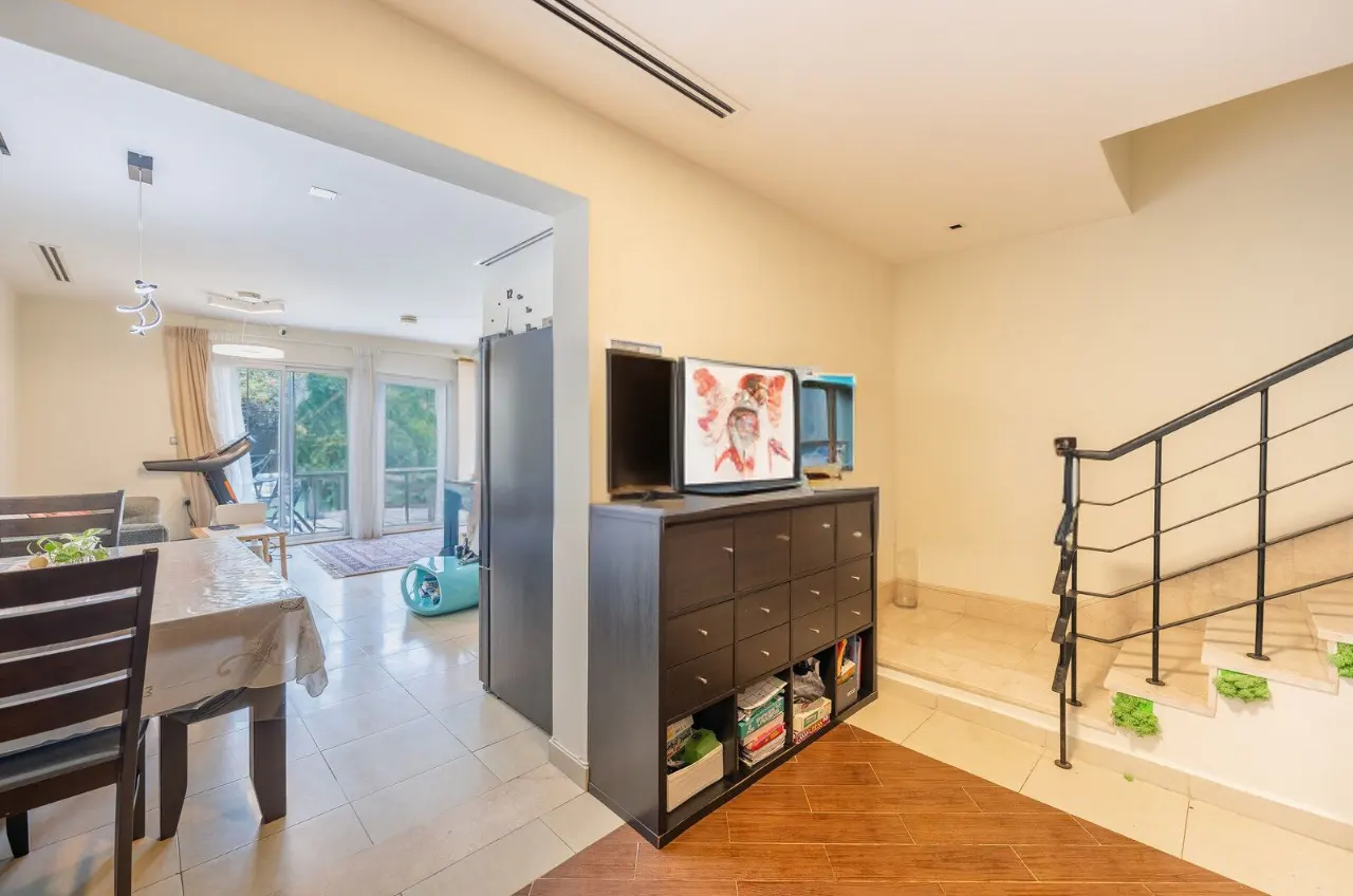 A view of a home interior with a dining area, a cabinet with a TV, and a staircase.