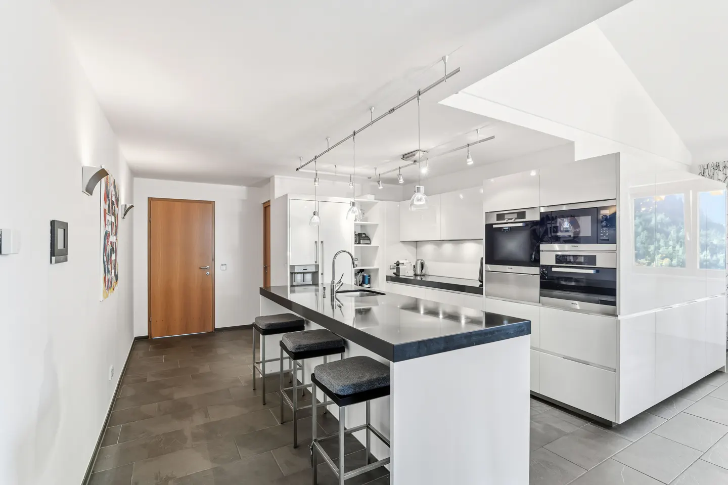 Bright, modern kitchen with white cabinets, black countertop island with three stools, and stainless steel appliances.