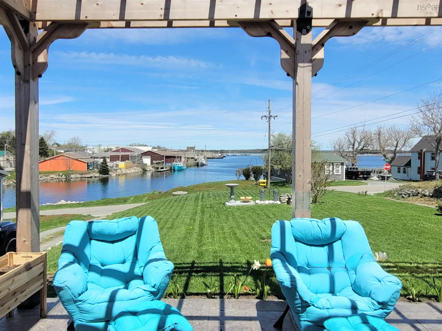 View from a pergola with two blue chairs overlooking a river, buildings, and a blue sky.