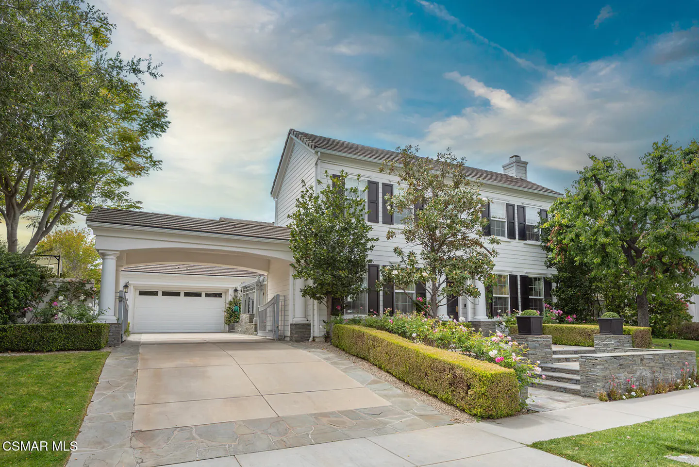 Exterior of a two-story white house with black shutters, a covered driveway, and manicured landscaping.