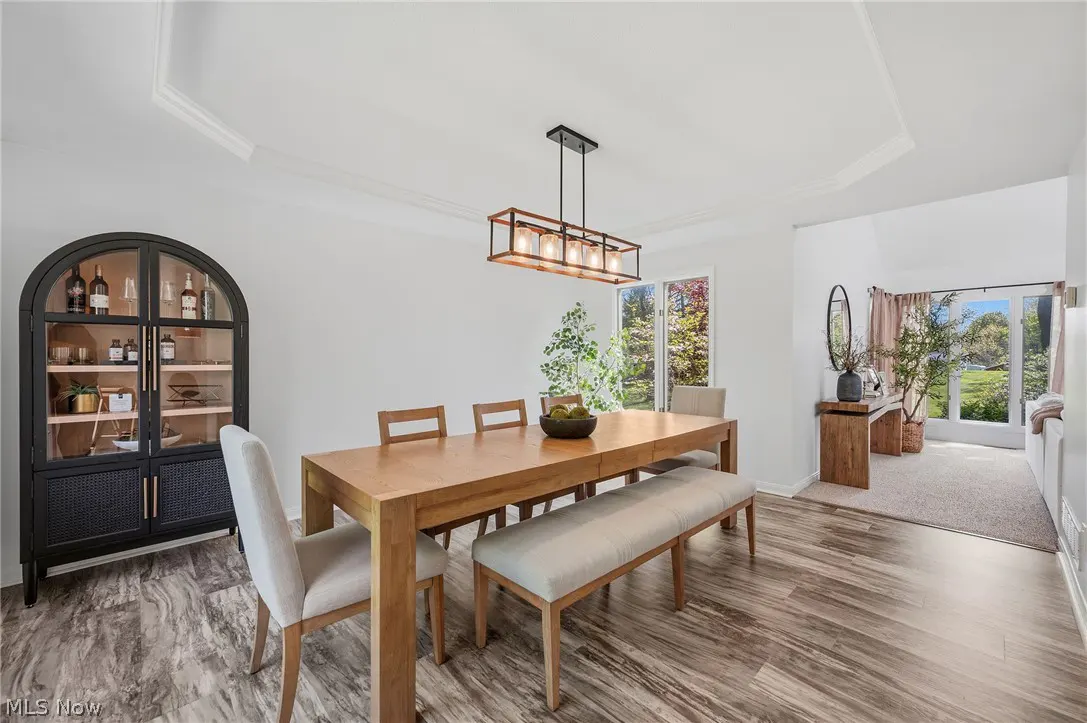 Bright dining room with wood table, bench, and chairs. A black cabinet displays glassware. A modern light fixture hangs above the table.