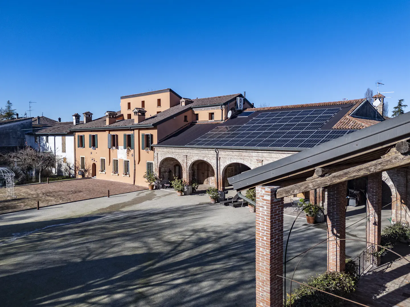 A sunny courtyard with a peach-colored building, arched brick walkways, and a roof covered in solar panels.