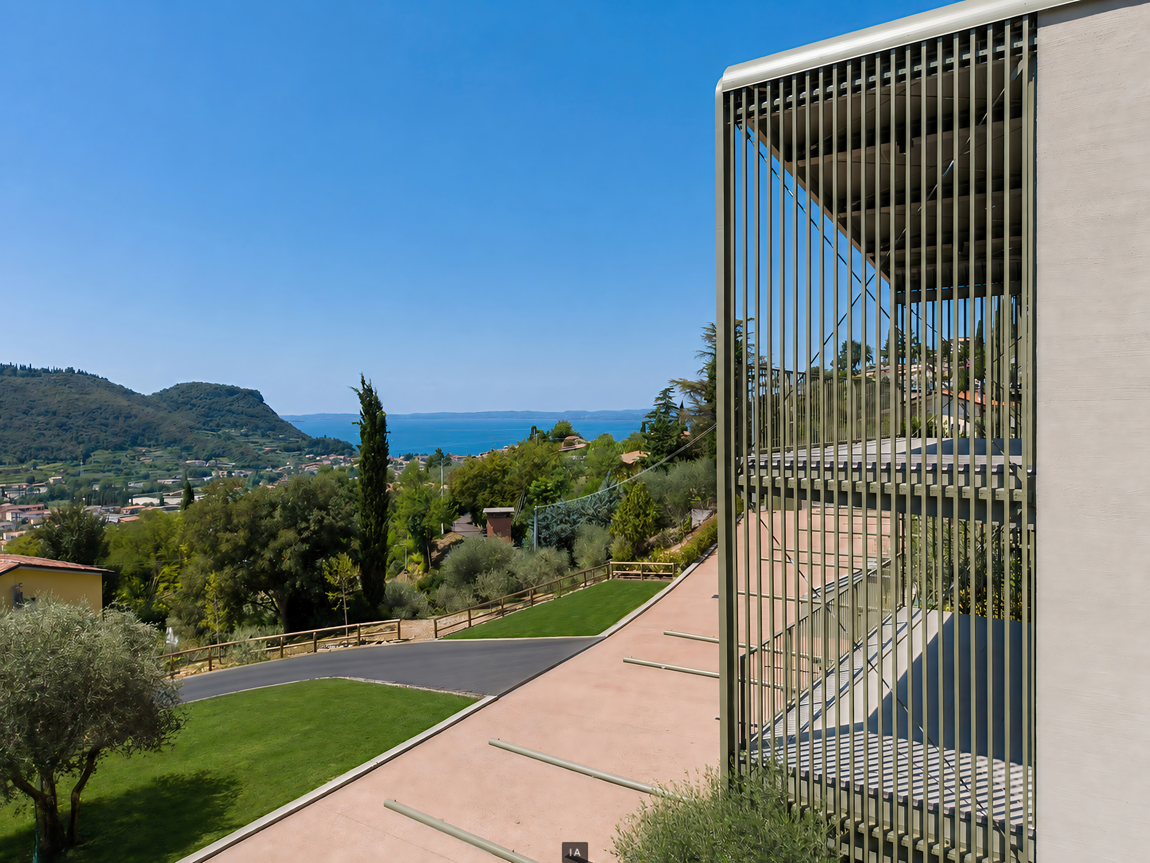 Modern building with green vertical slats overlooking a lush landscape, rolling hills, and a distant blue lake under clear sky. [AI-generated text]