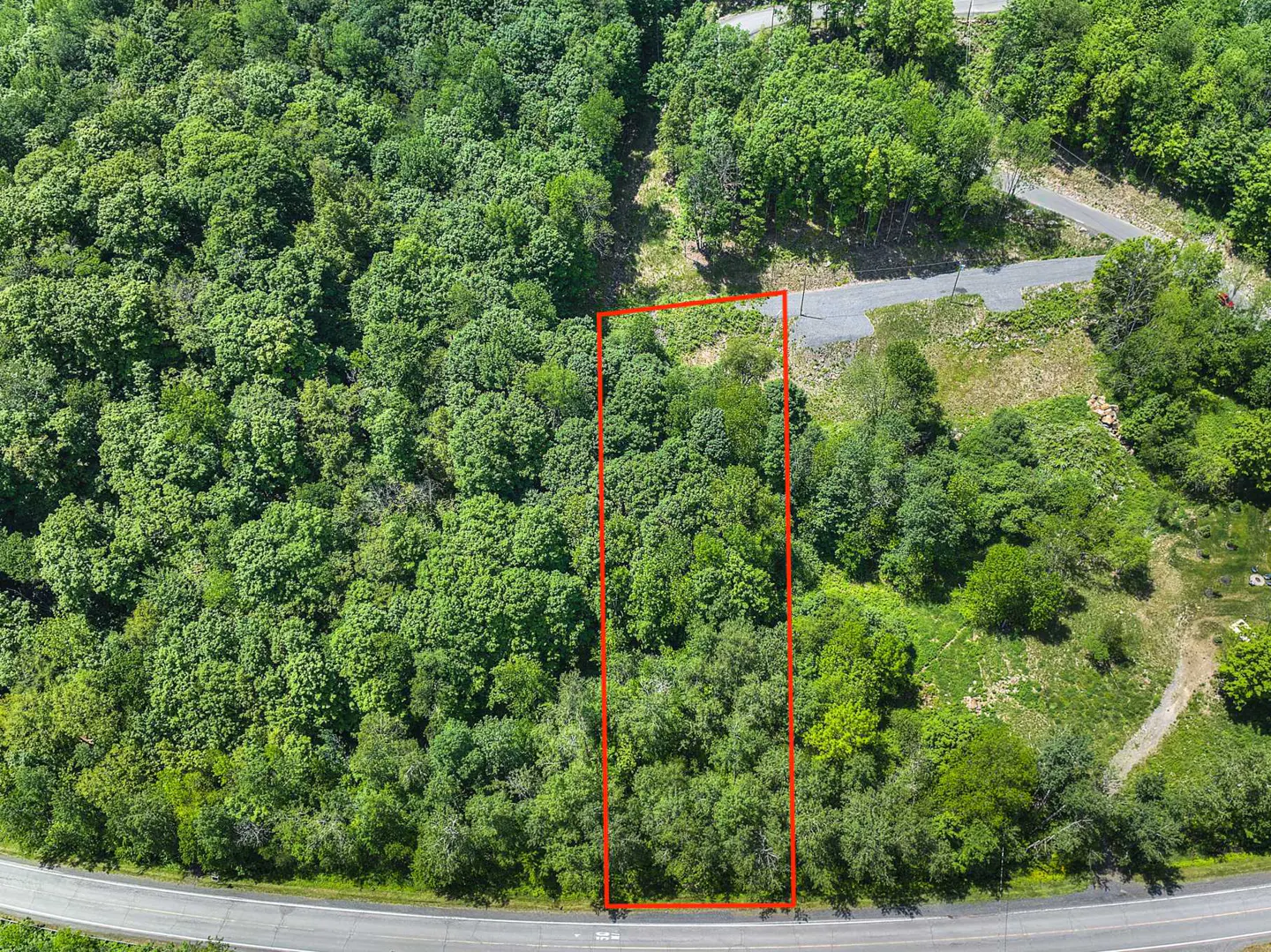Aerial view of a wooded lot outlined in red, next to a road and surrounded by dense green trees.