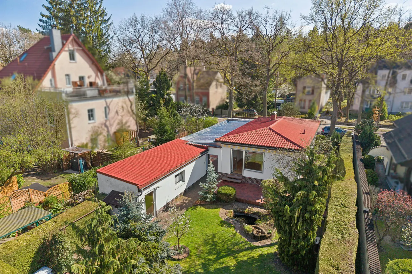 Aerial view of a white house with a red roof, surrounded by green trees and a well-maintained lawn.