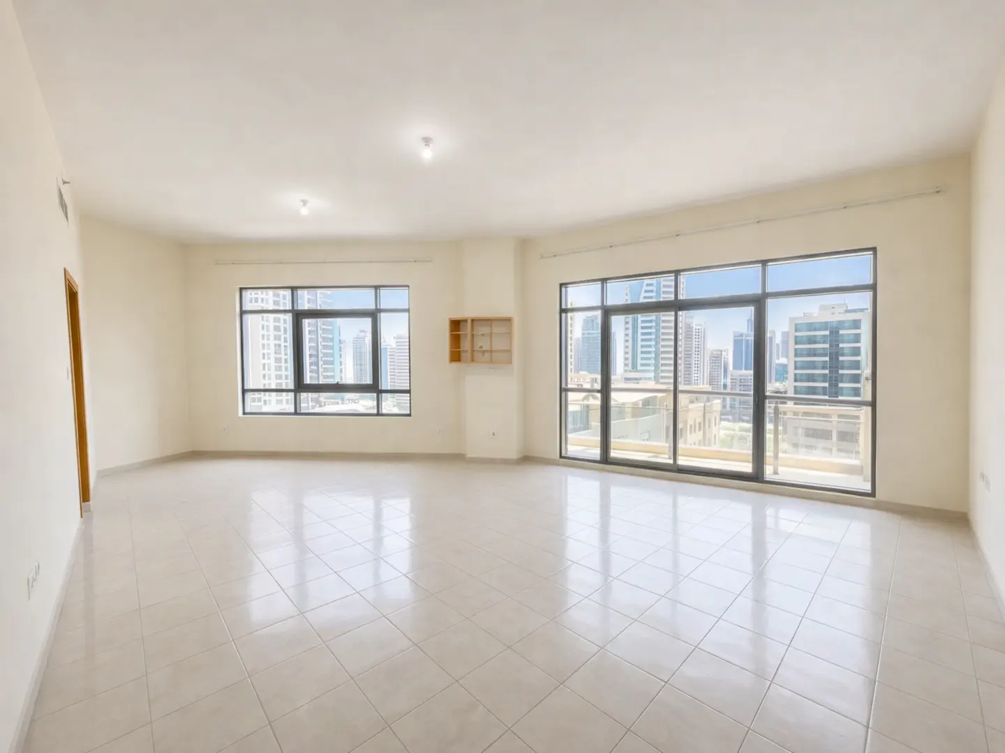 Bright, empty room with beige tile floor, white walls, and two large windows showing a city skyline.