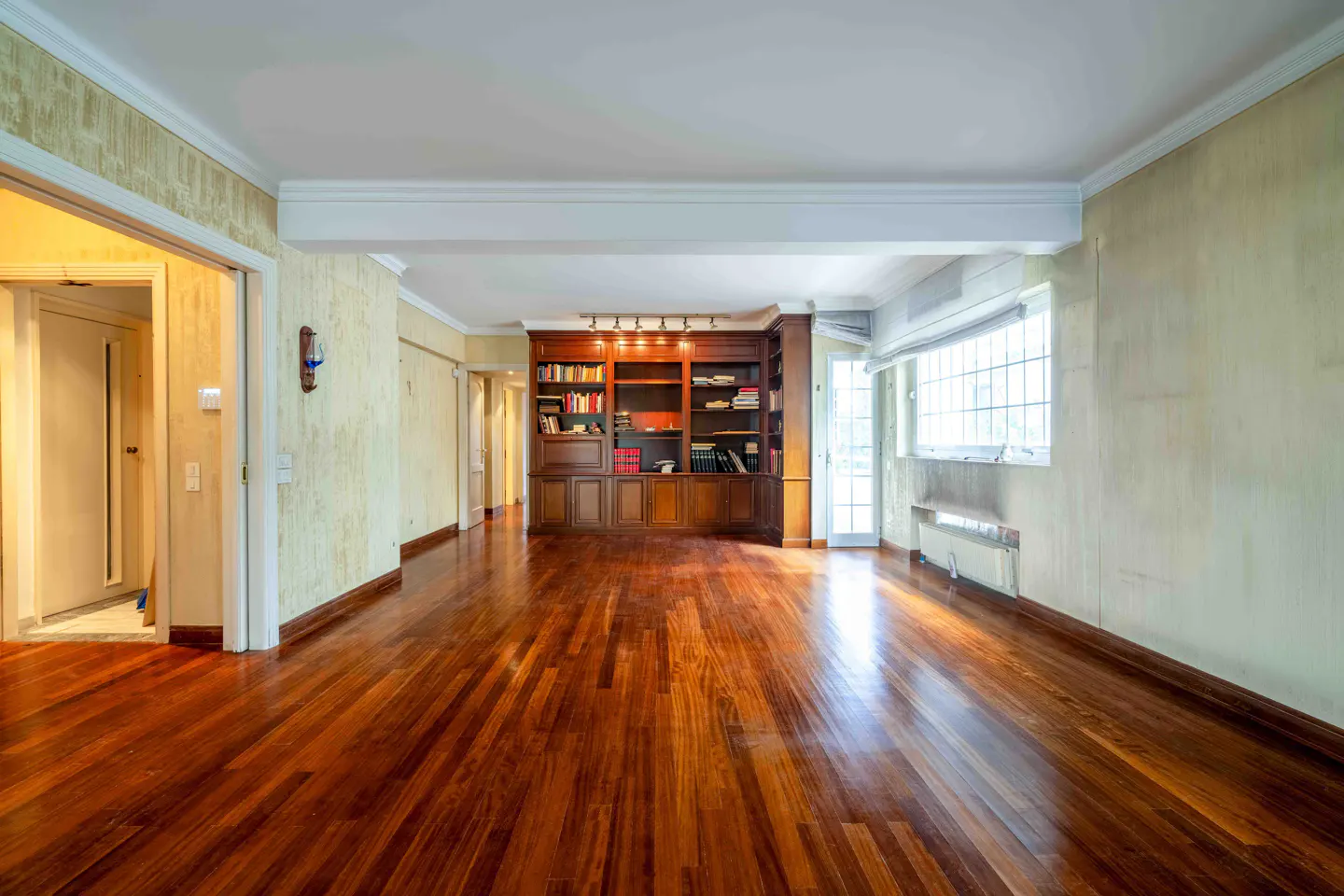 Spacious room with polished hardwood floors, light yellow walls, and a large built-in wooden bookcase at the far end.