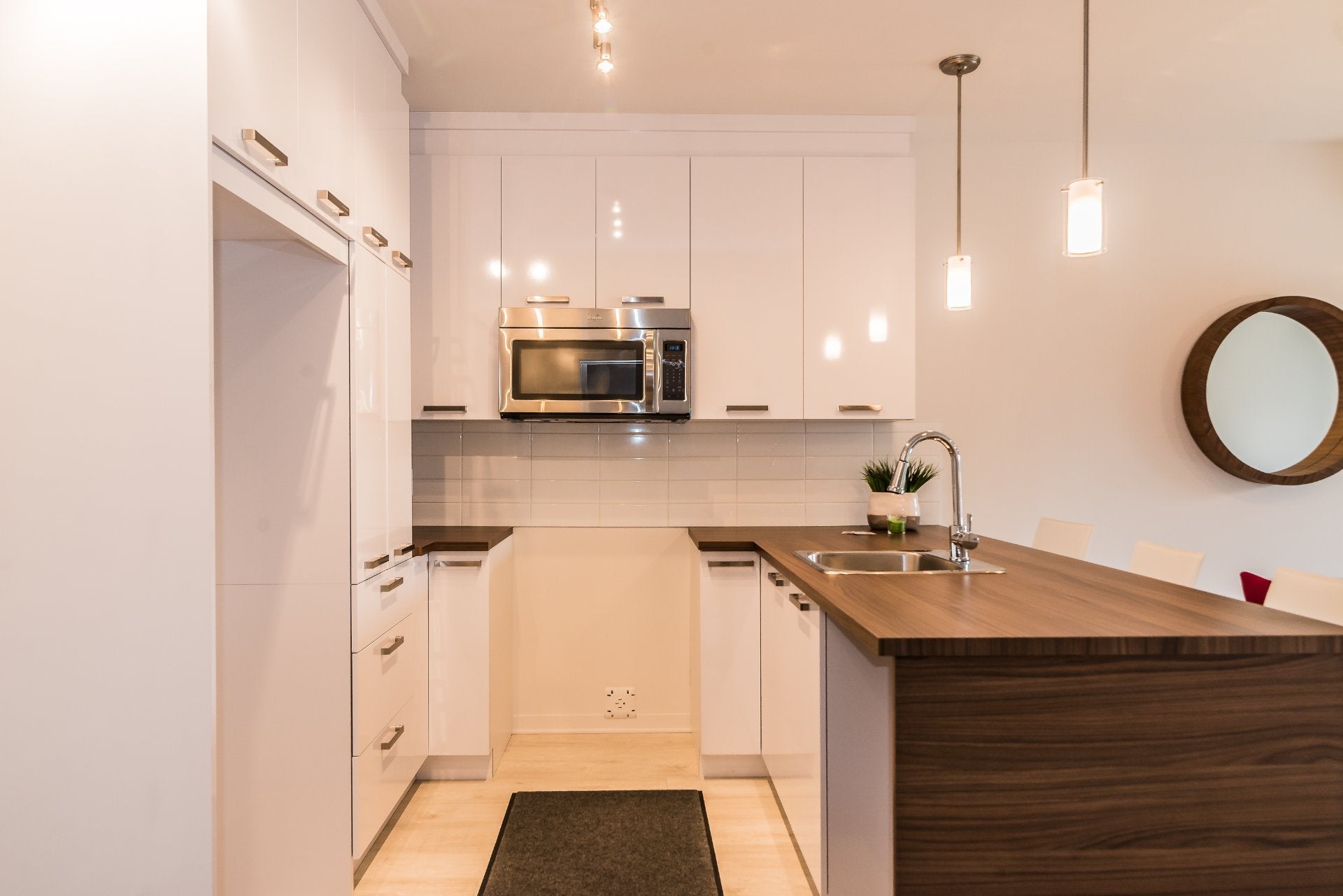 Modern kitchen with white cabinets, stainless steel microwave, dark wood island countertop, and a round wall mirror. [AI-generated text]