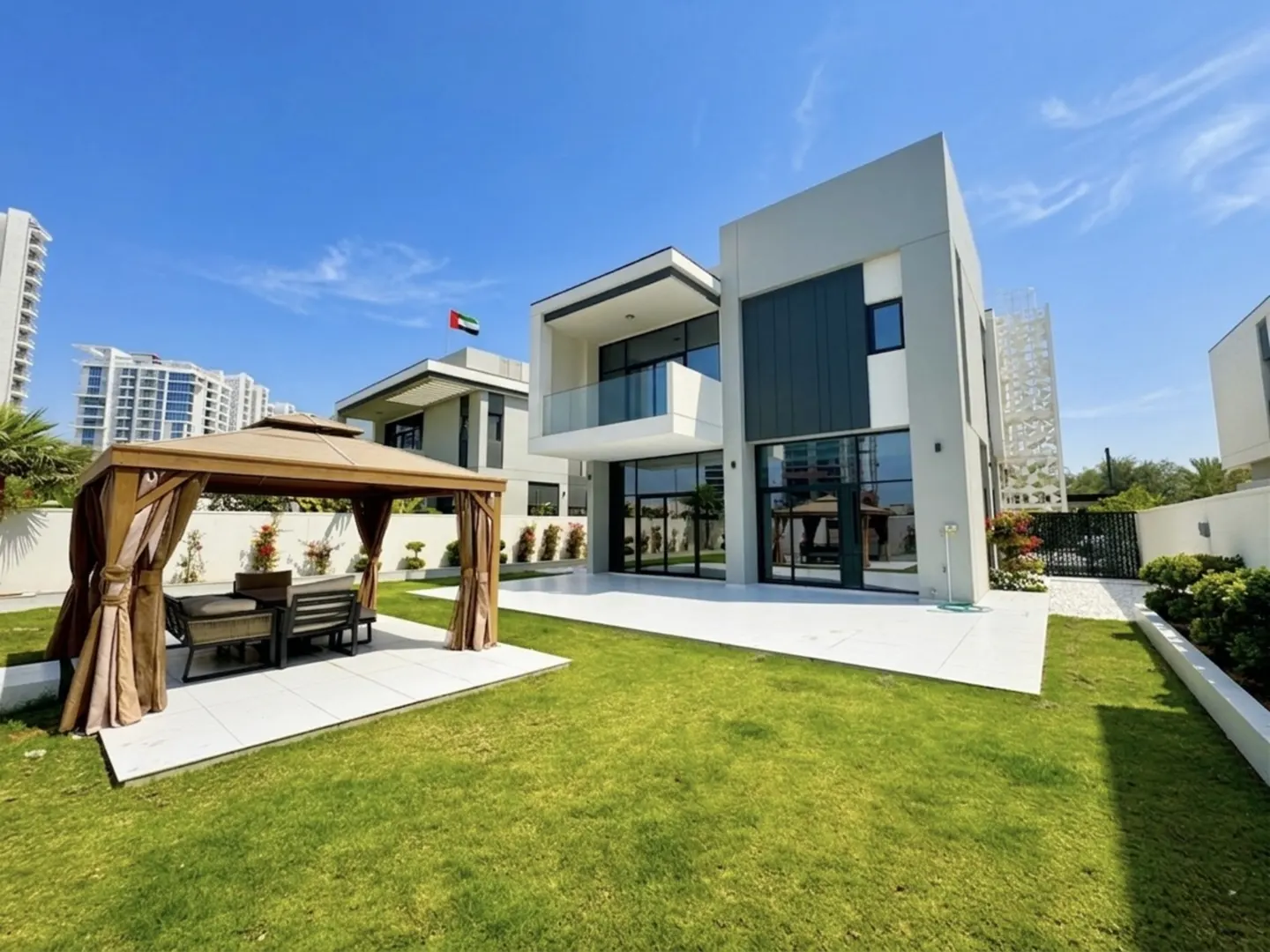 Modern two-story house with a green lawn, white patio, and a gazebo with brown curtains and furniture.