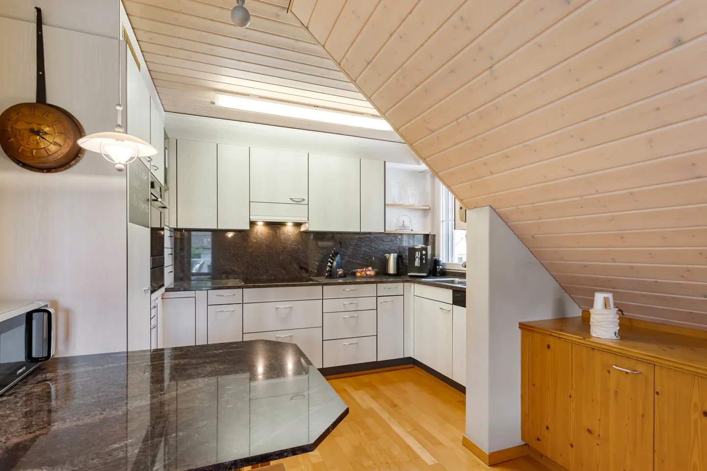 A kitchen with white cabinets, black countertops, and a wood ceiling. A dark granite island is in the foreground.
