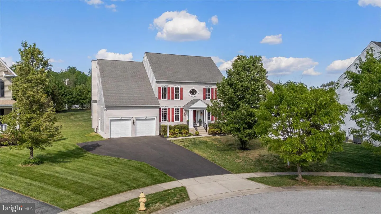 Two-story house with gray roof, light siding, red shutters, and two-car garage on a sunny day.