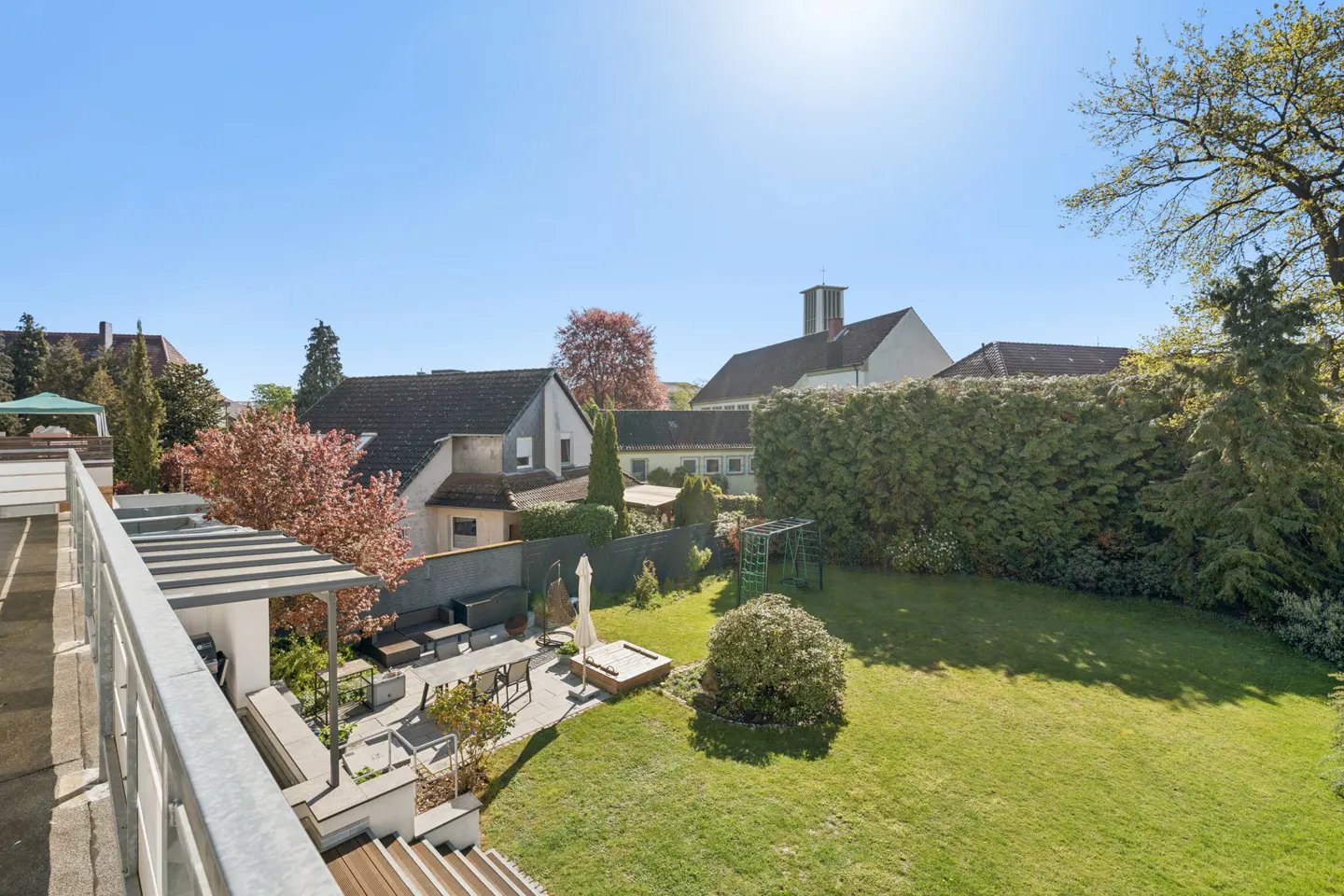 View of a green lawn, patio with furniture, and houses under a blue sky.