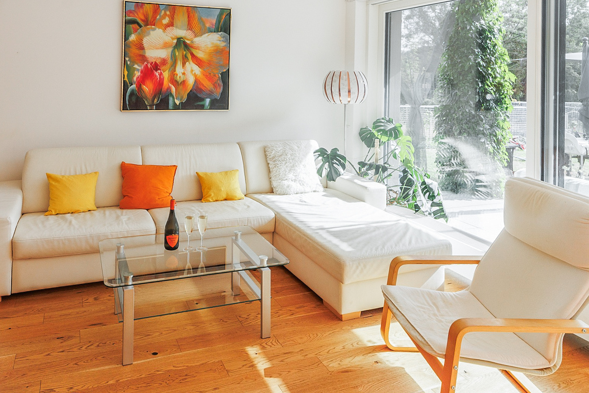 Bright living room with a white sectional sofa, colorful pillows, glass coffee table, and a large window overlooking a garden. [AI-generated text]