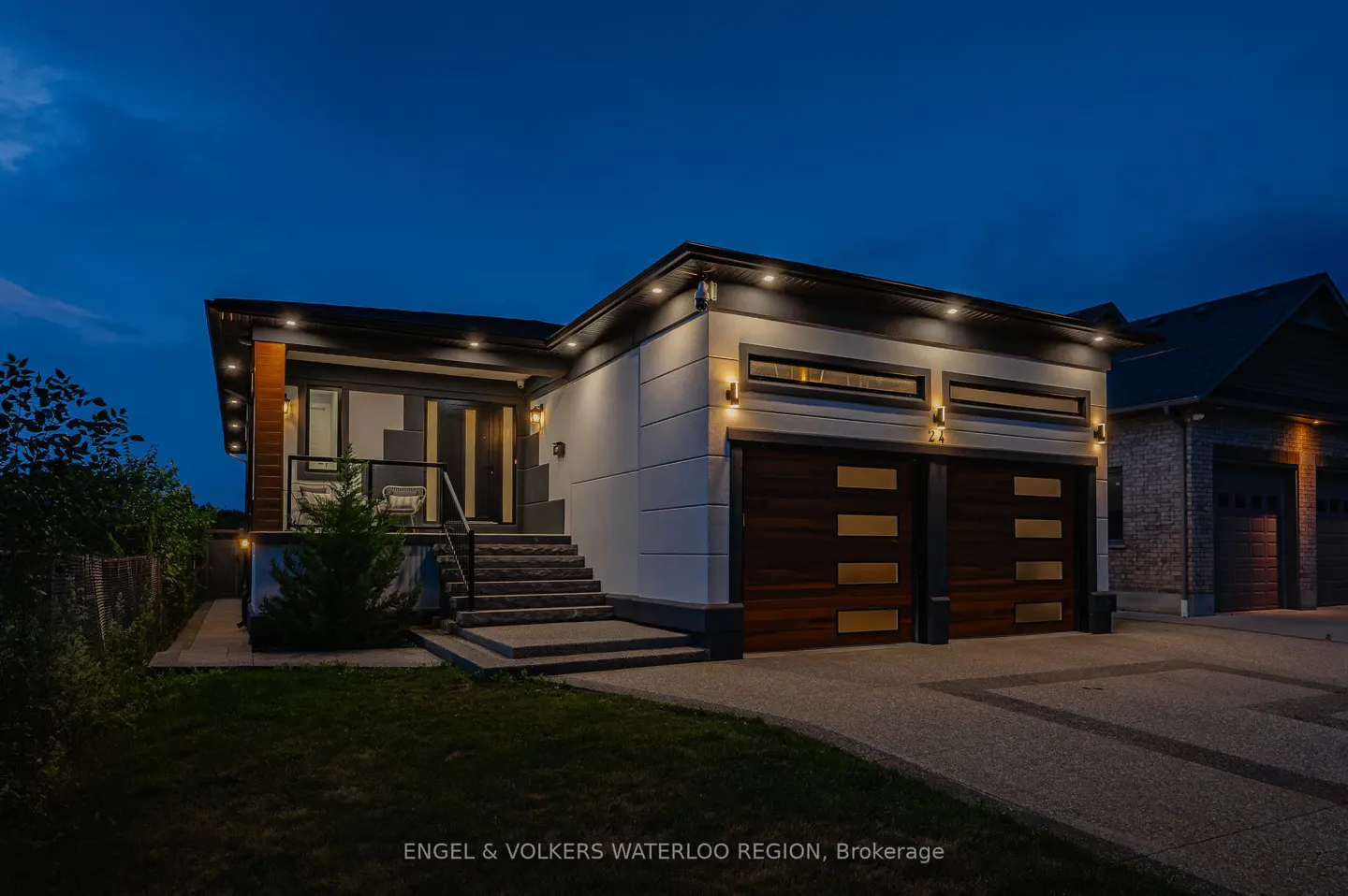 Exterior shot of a modern, one-story home at dusk with a two-car garage, stone steps, and manicured lawn.