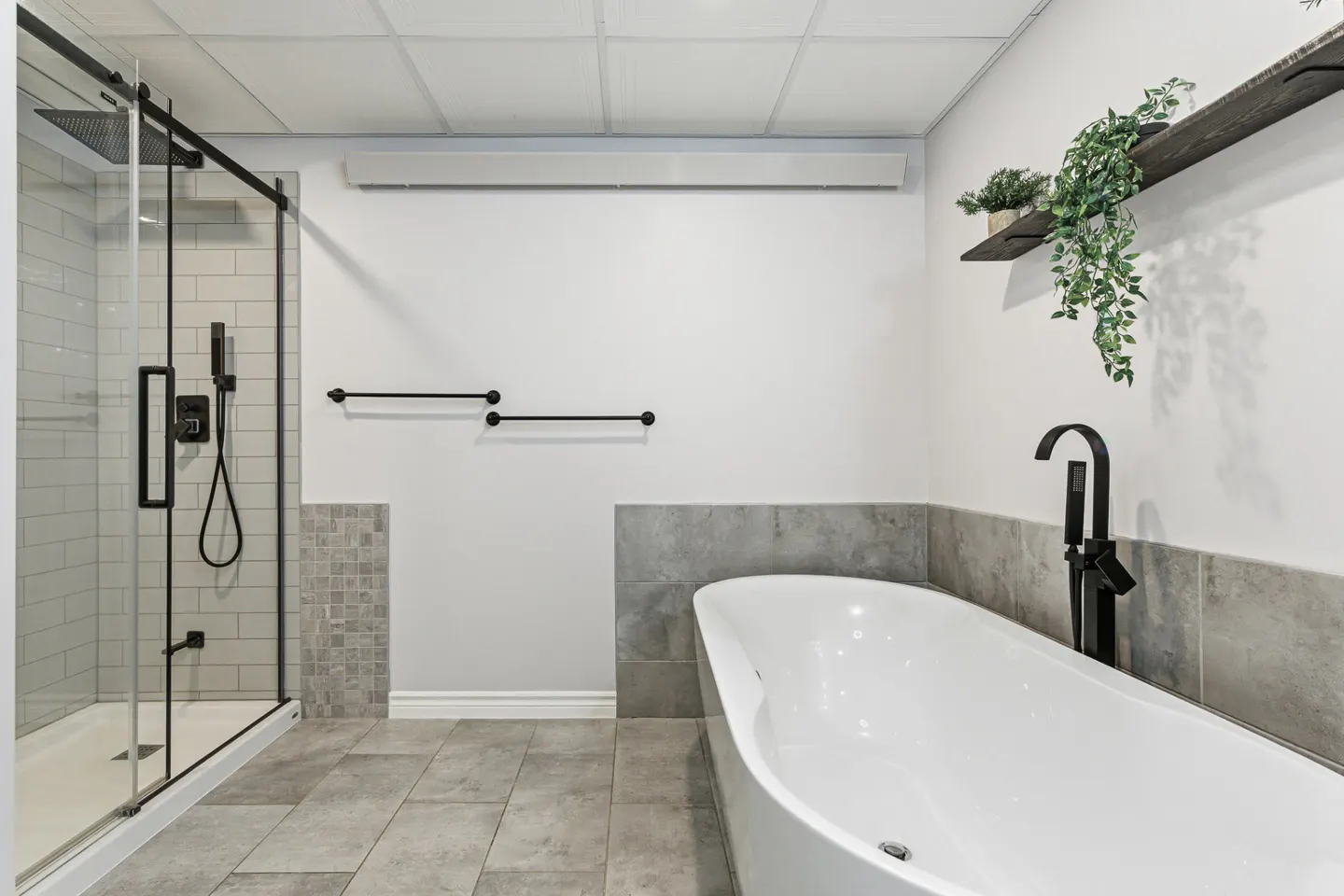Modern bathroom with white walls, gray tile floor, a glass shower with black trim, and a white freestanding tub.