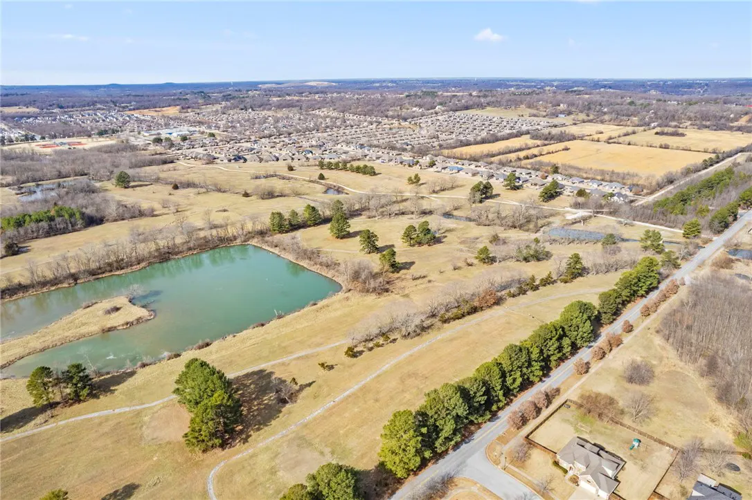 Aerial view of a neighborhood with a pond, fields, and trees under a blue sky.