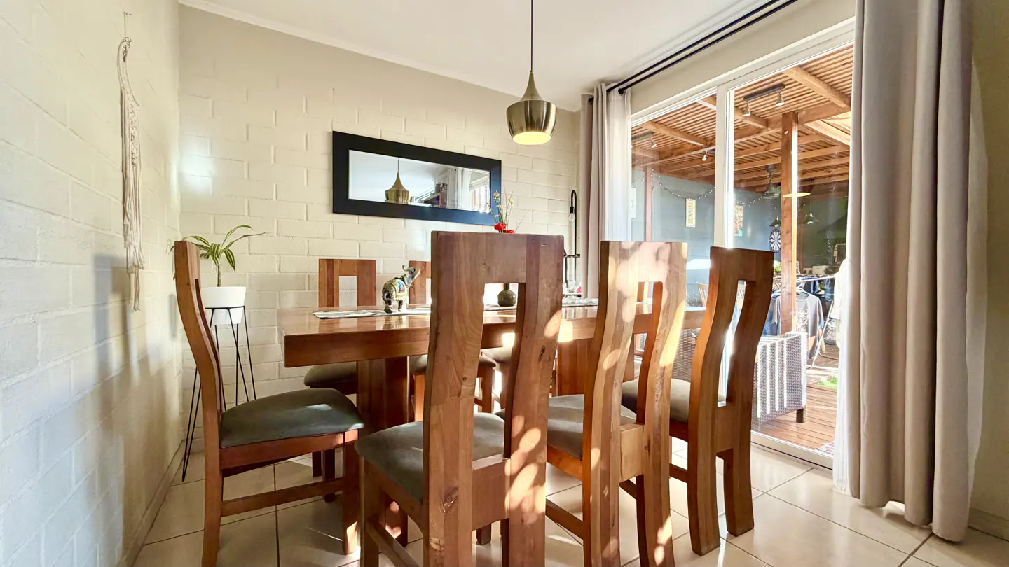 A dining room with a wooden table and chairs, a pendant light, and a sliding glass door to an outdoor patio.