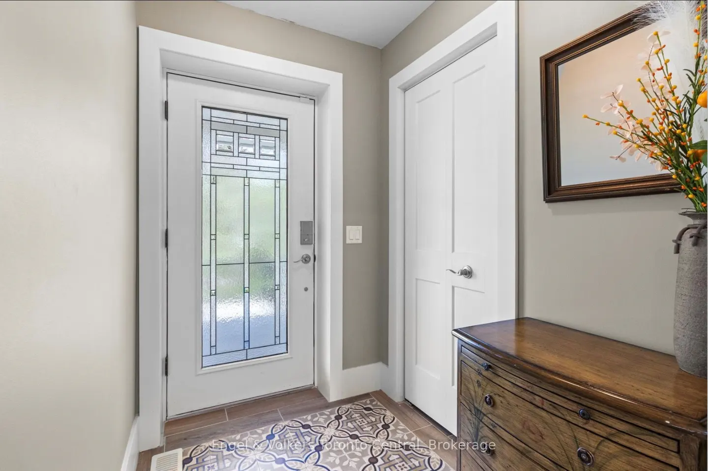 Entryway with a white door with glass panels, a white closet door, and a wooden dresser with a vase of flowers.