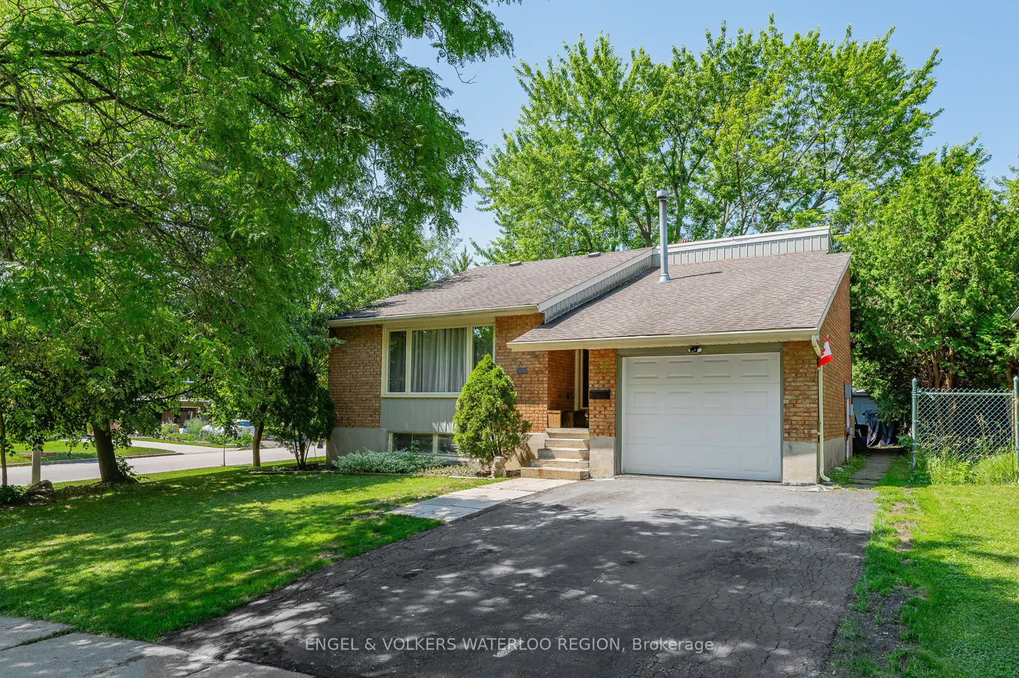 A single-story brick house with a white garage door, green lawn, and trees.