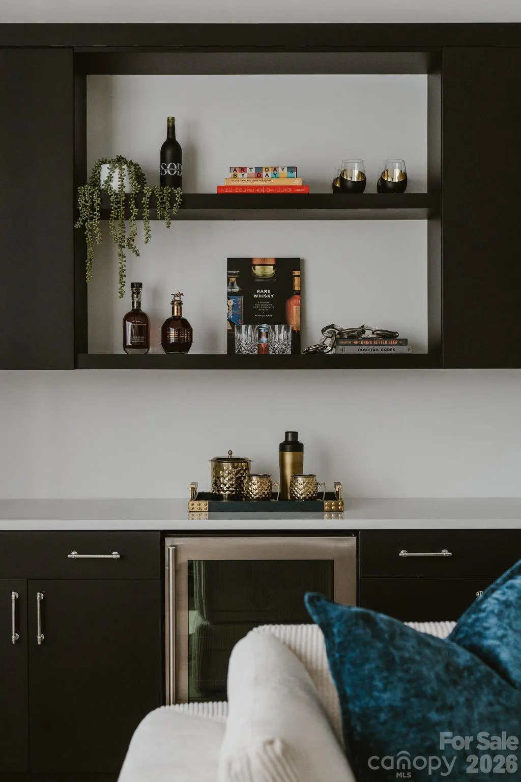 Modern black cabinetry with open shelving displaying books, a trailing plant, and barware above a built-in wine fridge.
