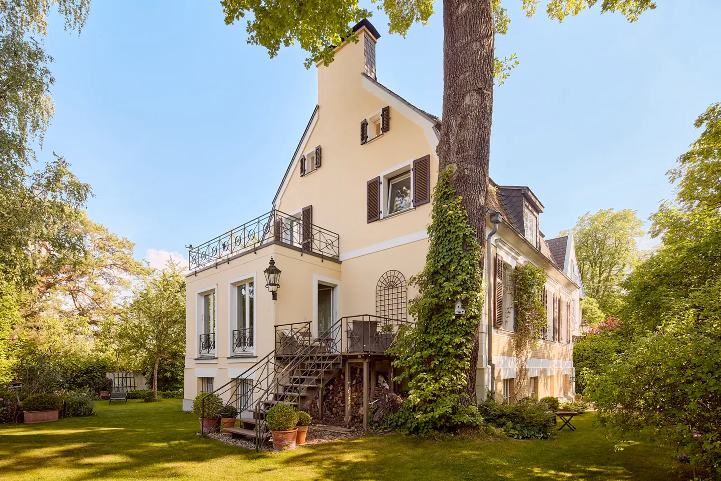 Exterior view of a yellow two-story house with brown shutters, a black iron balcony, and a green lawn.