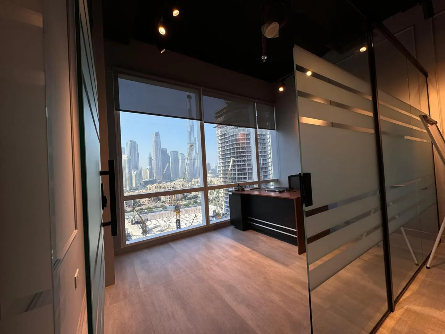 Office space with a large window view of a city skyline. A desk sits near the window, and glass walls divide the space.