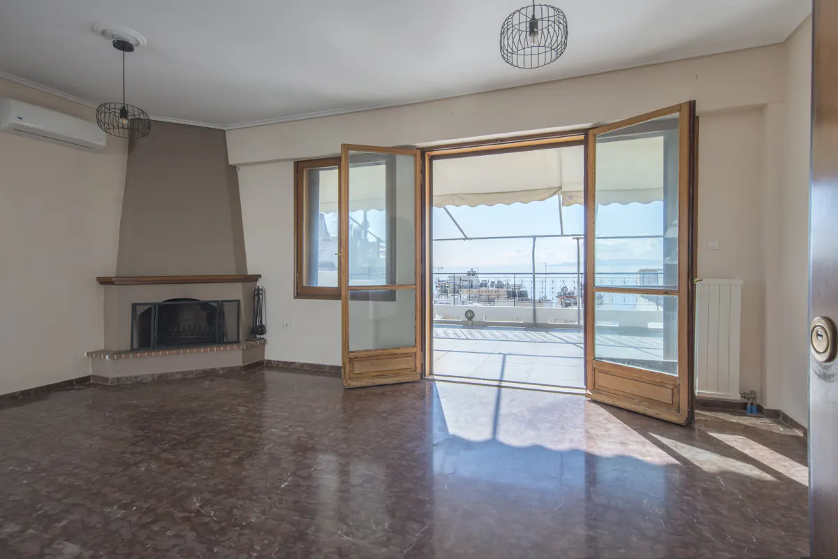A bright living room with a fireplace, marble floors, and open doors leading to a balcony with a sea view.