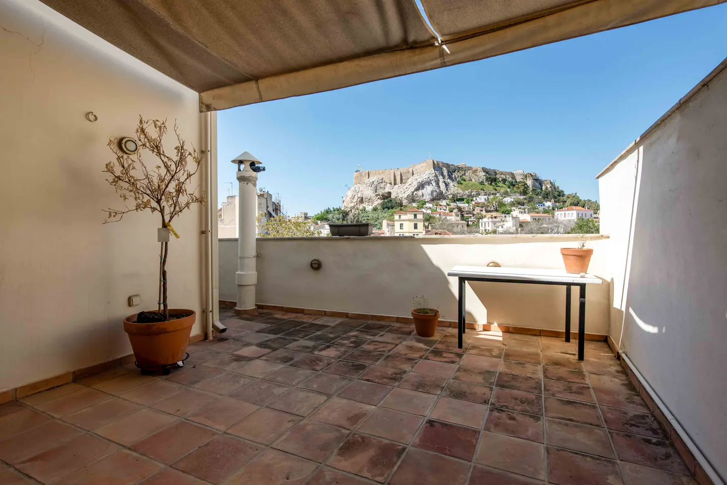 A rooftop terrace with terracotta tiles, a small table, and a view of the Acropolis in Athens.