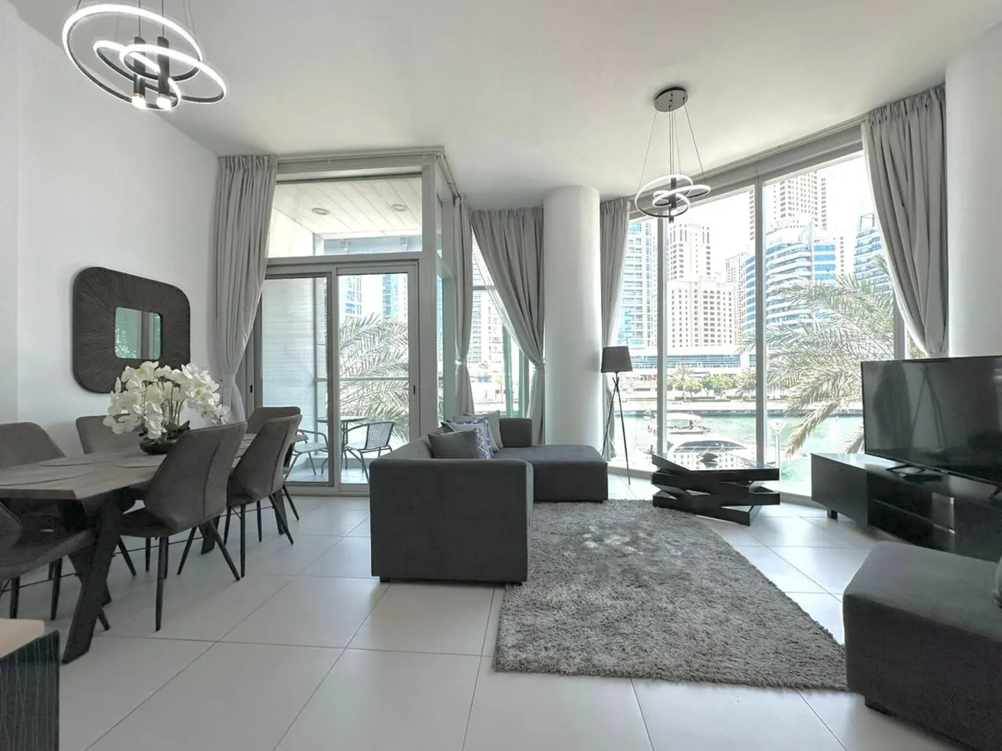 Bright, modern apartment interior with gray furniture, dining table, and city view through large windows.