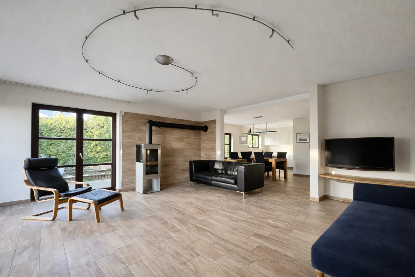 A bright living room with a black leather sofa, a wood-burning stove, and a black chair with a footstool.