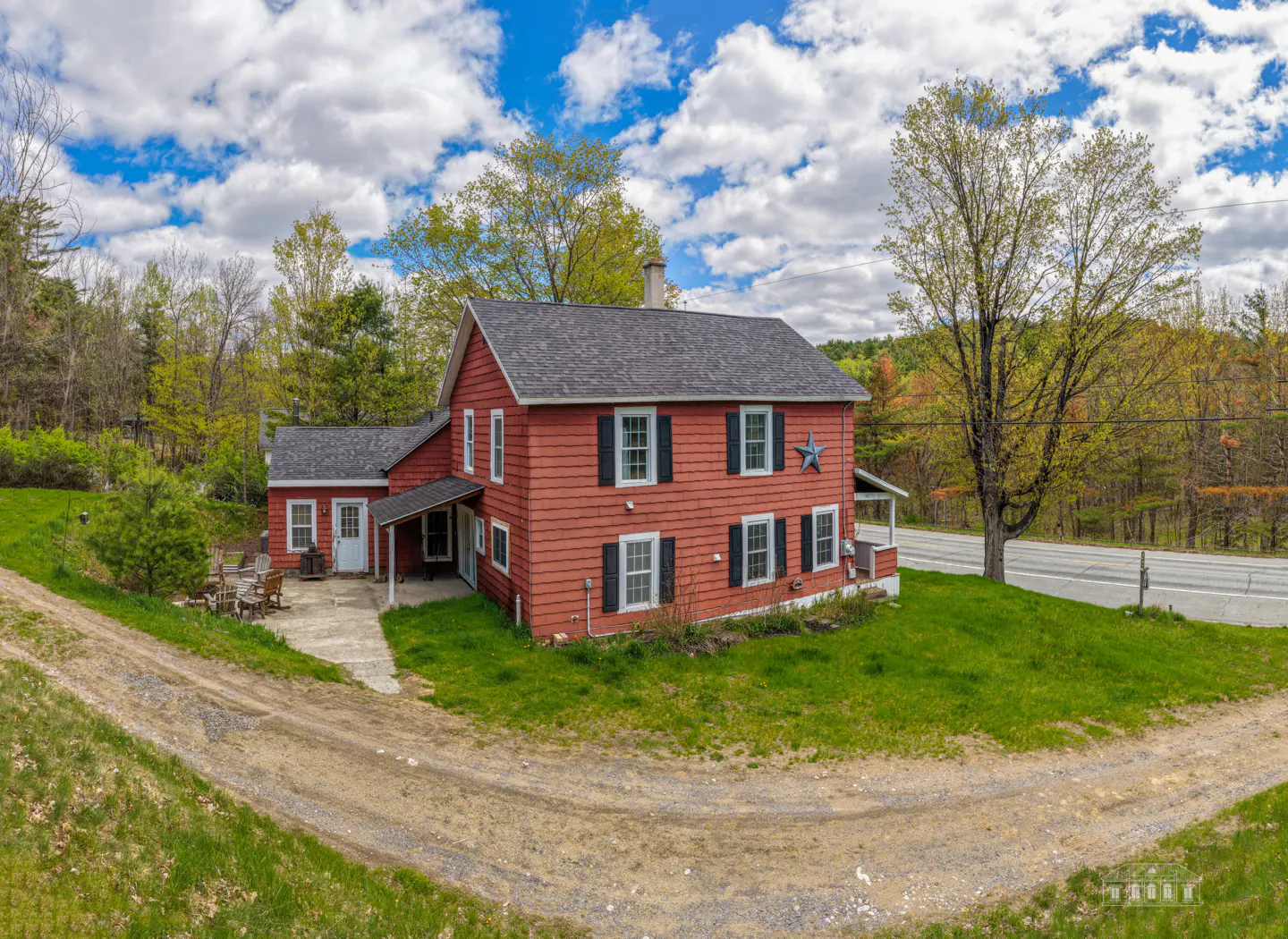 Two-story red farmhouse with black shutters, gray roof, and a blue star on the front. Green lawn and trees surround the house.