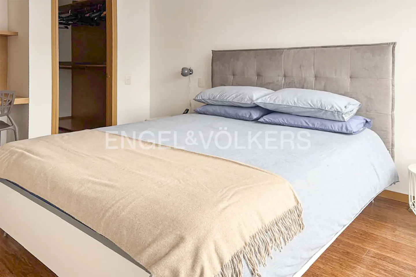 Bedroom with a gray headboard, blue bedding, and a tan throw blanket. A closet is visible in the background.