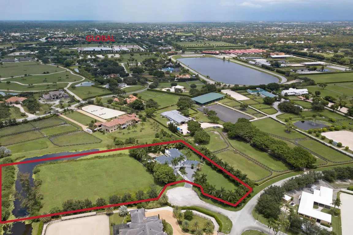 Aerial view of a large property outlined in red, featuring a house, pond, and green fields in a lush, upscale neighborhood.