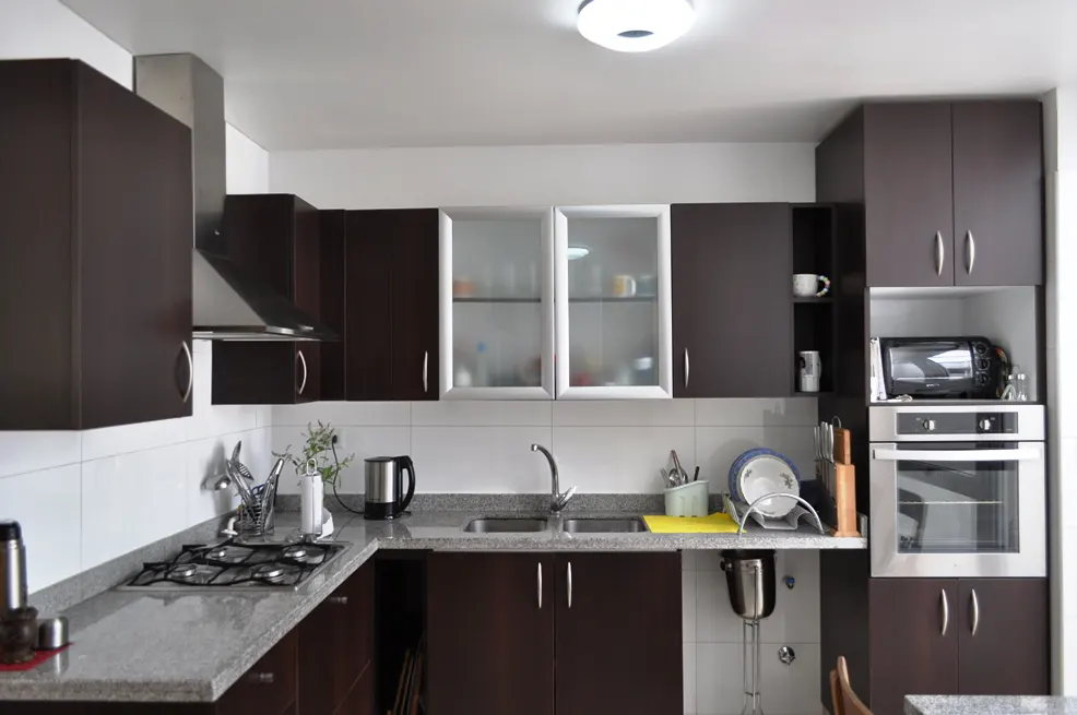 A modern kitchen with dark brown cabinets, stainless steel appliances, and white tile backsplash.