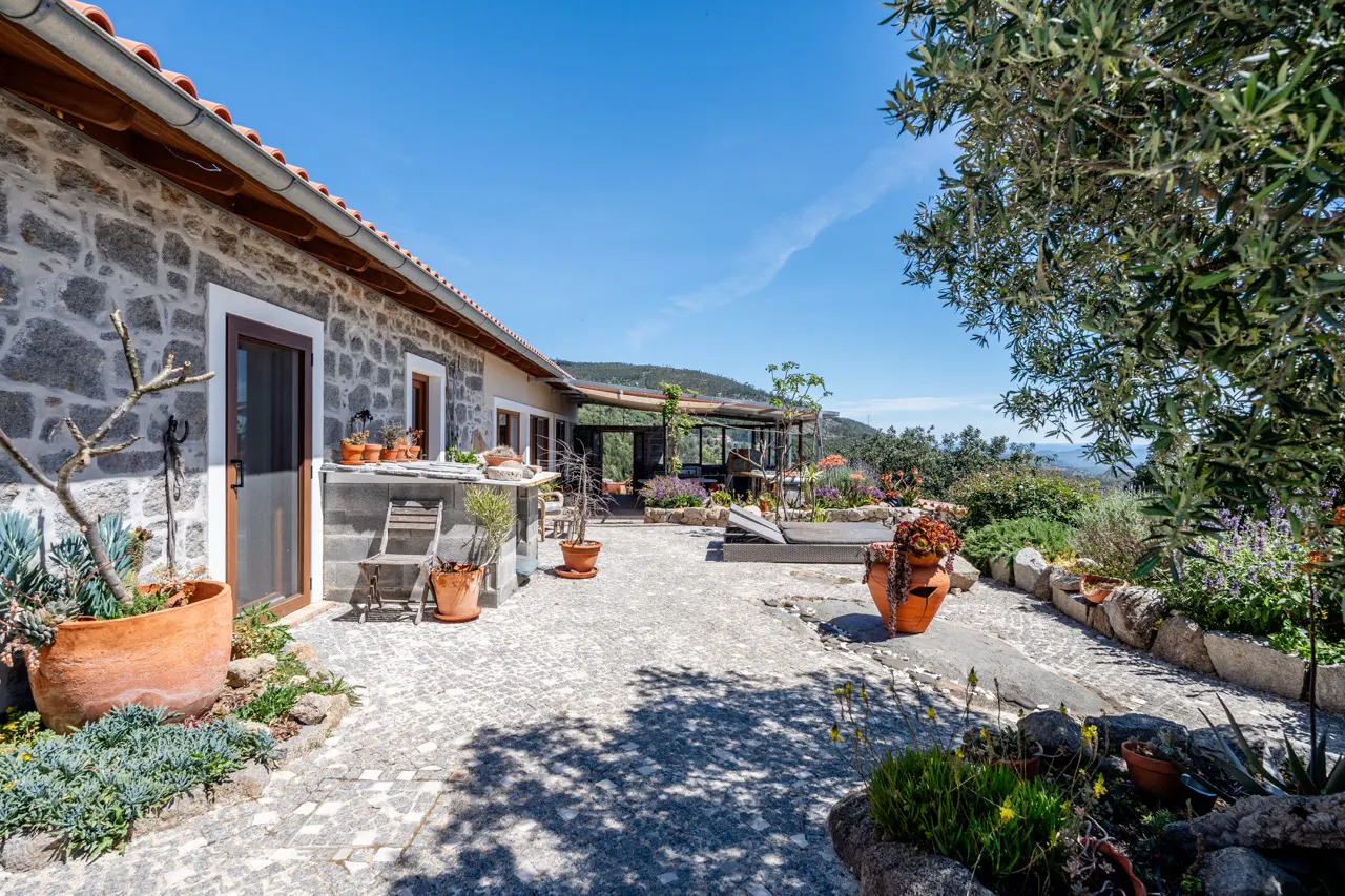 Stone house with a patio, potted plants, and a view of the mountains under a blue sky.