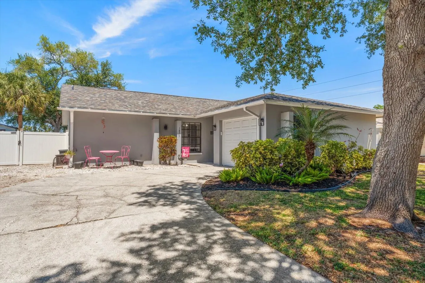 Exterior view of a gray single-story home with a white garage door and a concrete driveway. A pink bistro set sits on the left.