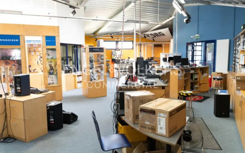 A commercial space with display cases, desks, and boxes. The walls are painted in blue and orange. A Korg banner hangs in the background.