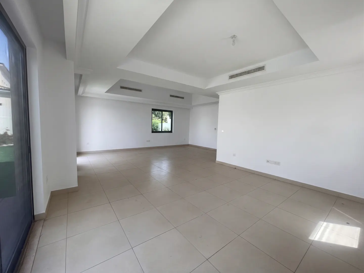 An empty, bright room with white walls, beige tile floor, and a window.