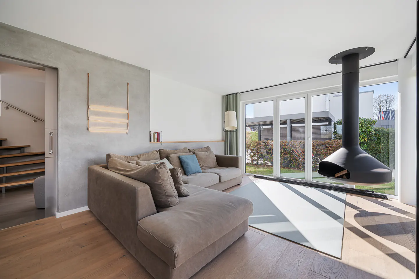 Living room with a gray sectional sofa, a modern hanging fireplace, and sliding glass doors to a garden.