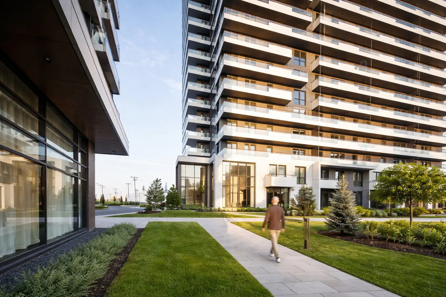 A man walks on a stone path toward a modern high-rise apartment building with balconies and green landscaping.