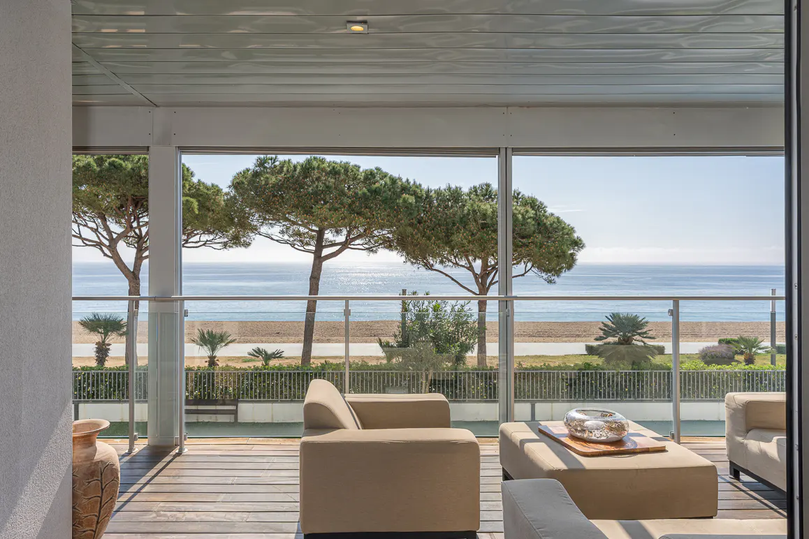 Balcony with tan seating overlooks the ocean. Trees line the beach.