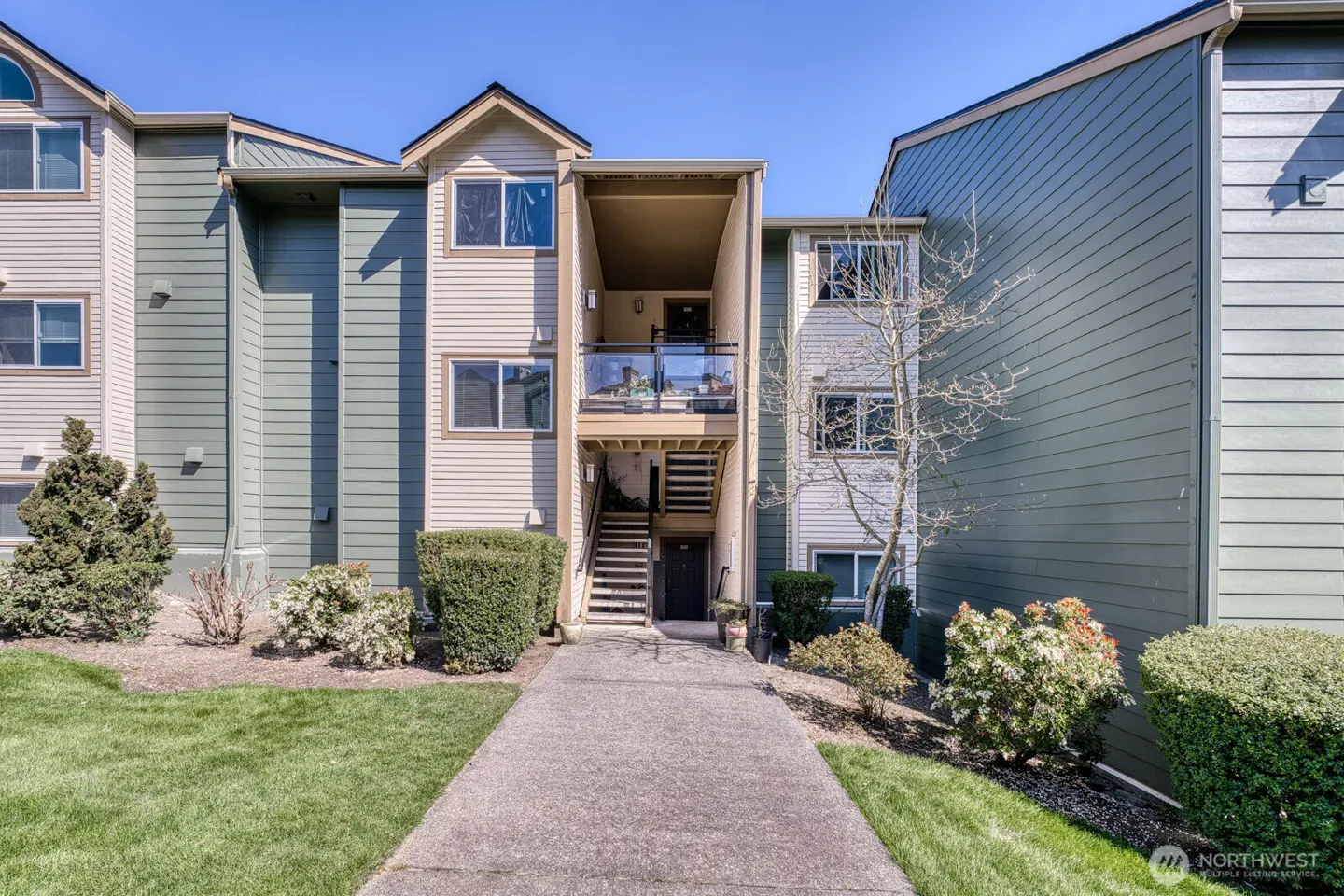 Exterior of a three-story apartment building with green and beige siding, a walkway, and green lawn.