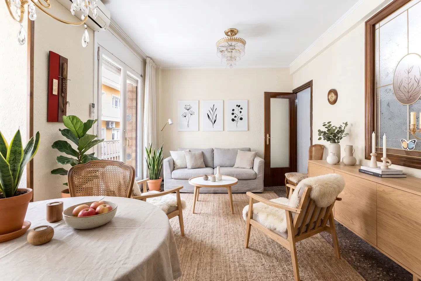 A bright living room with a round table, sofa, chairs, and a wooden cabinet. Plants and decorative items add a touch of nature and elegance.