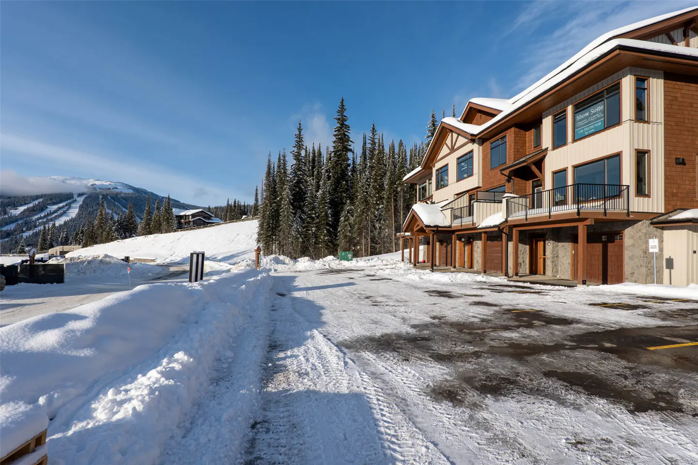 Exterior view of a brown and beige condo building with snow-covered ground and evergreen trees under a blue sky.