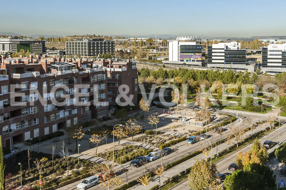 Real estate view of brick apartments, office buildings, and a park under a blue sky. Cars line the street with trees. Engel & Volkers logo overlay.