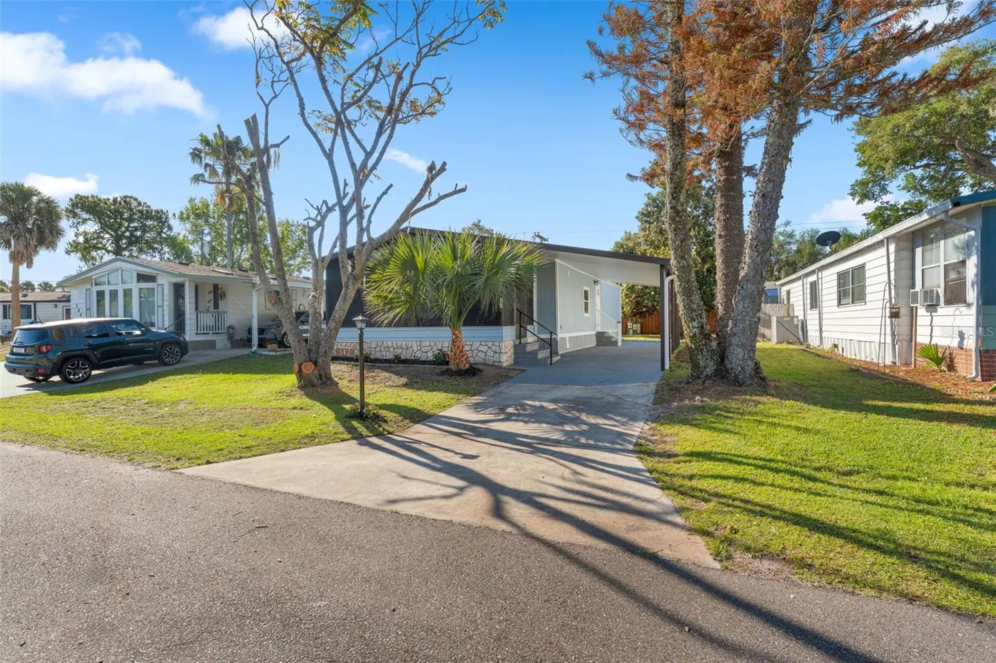 Exterior view of a light blue single-story home with a carport and a paved driveway on a sunny day.