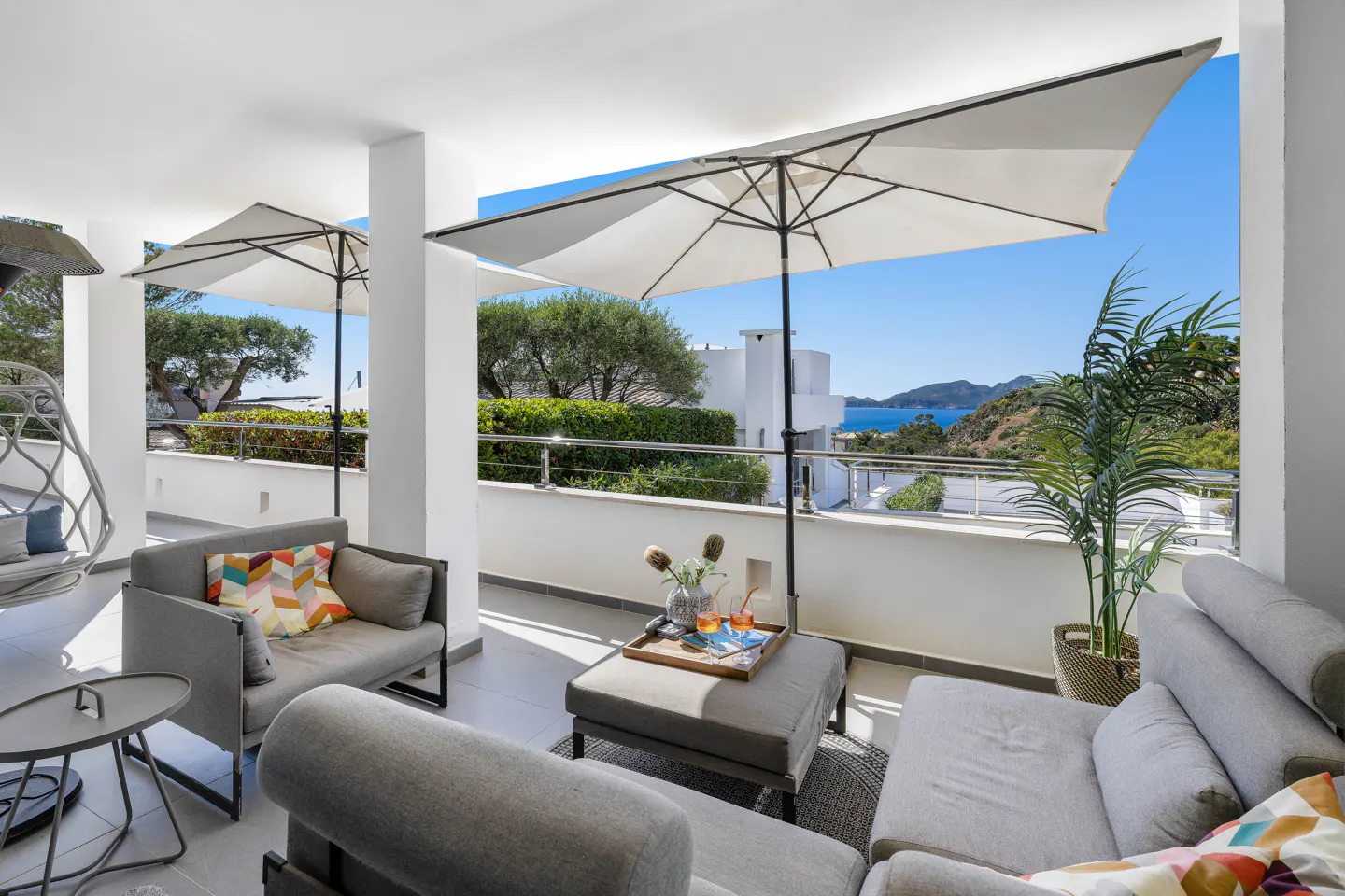 A covered patio with gray furniture, white umbrellas, and a view of the ocean.