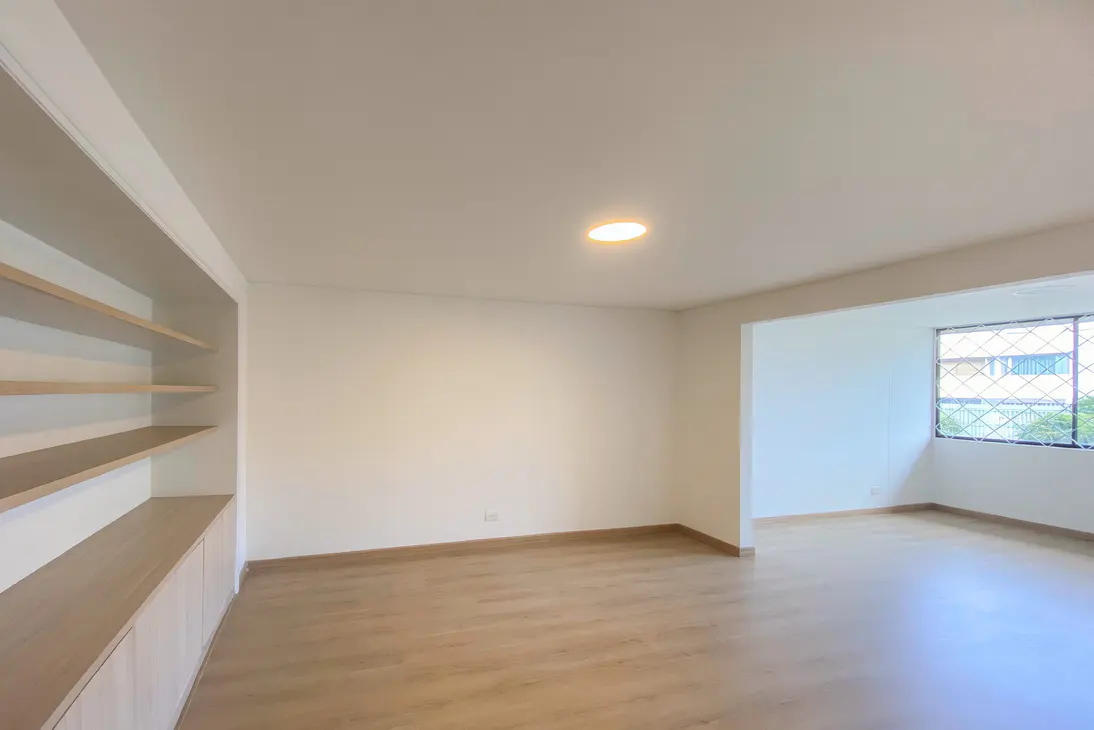 Bright, empty room with light wood floors, white walls, and built-in shelves. A window lets in natural light.