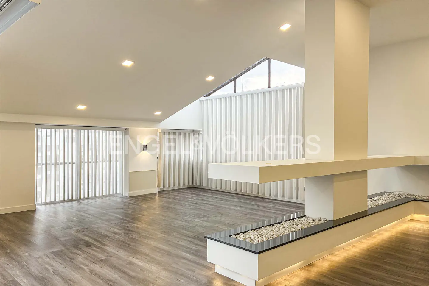 Bright, modern living room with wood floors, white walls, and vertical blinds. A white fireplace with stones adds a unique touch.