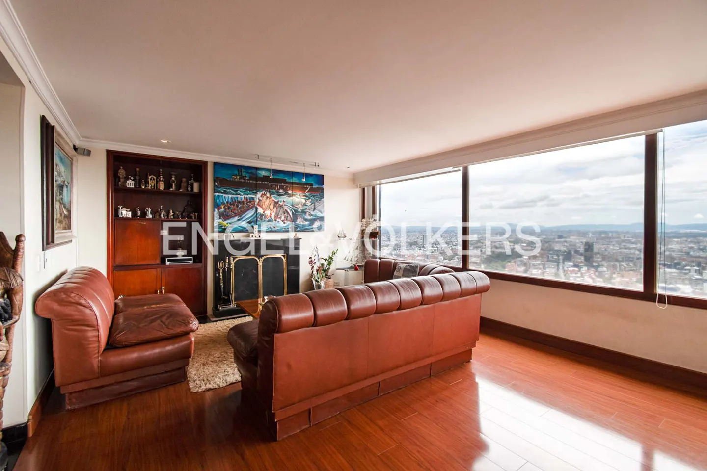 A living room with brown leather sofas, a fireplace, and a large window overlooking a city.